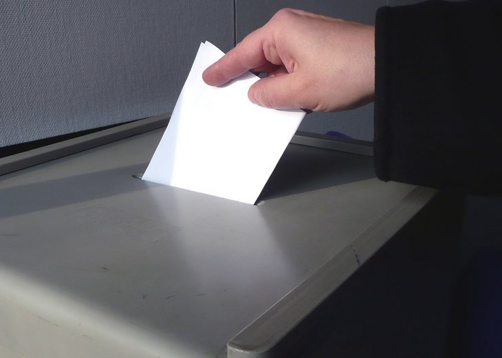 Eine Hand schiebt einen Zettel in eine Wahlurne.