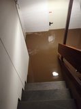Treppenabgang in den Keller, ab der ersten Treppenbiegung steht alles unter Wasser, es sieht aus, als würde man in einen Pool steigen, aber das Wasser ist schlammig-braun.